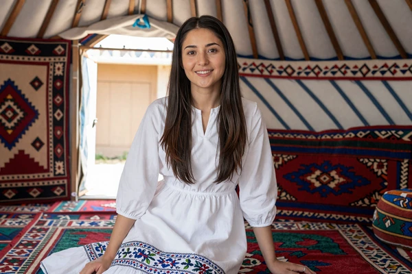 Kyrgyz woman sitting inside a traditional yurt decorated with colorful shyrdak felt carpets, representing the rich nomadic heritage of Kyrgyz women dating culture