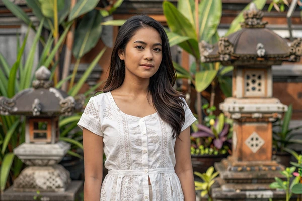 Young Indonesian Javanese woman in modern batik-print dress standing in traditional Javanese garden, representing diverse Indonesian dating culture