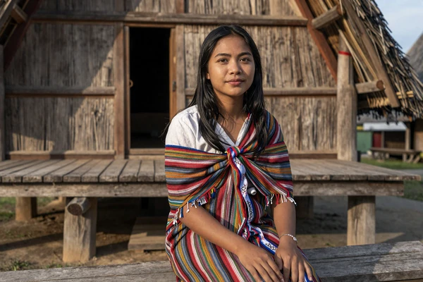 Timorese woman wearing traditional tais textile near a sacred house, representing the cultural heritage of Timorese women dating